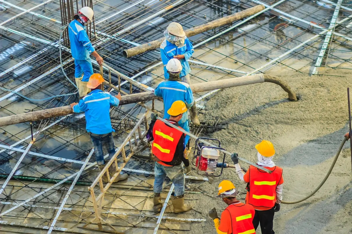 Construction crew in hard hats pouring concrete over rebar on a commercial job site